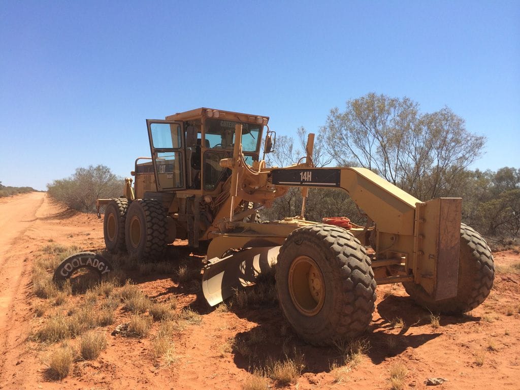 Cat 14H motor grader on a red bush track with scrub behind