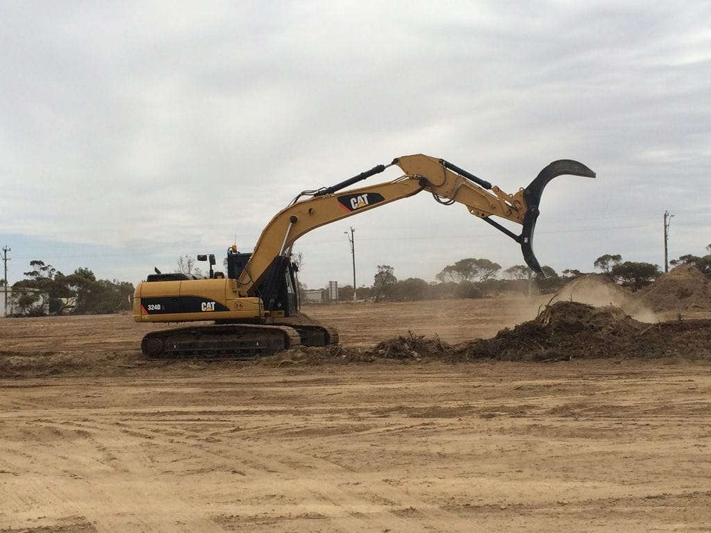Cat 320D excavator with a rake attachment clearing scrub on a cleared pad