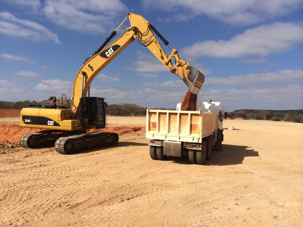 Cat 324D excavator loading a white end tipper truck on a red dirt pad