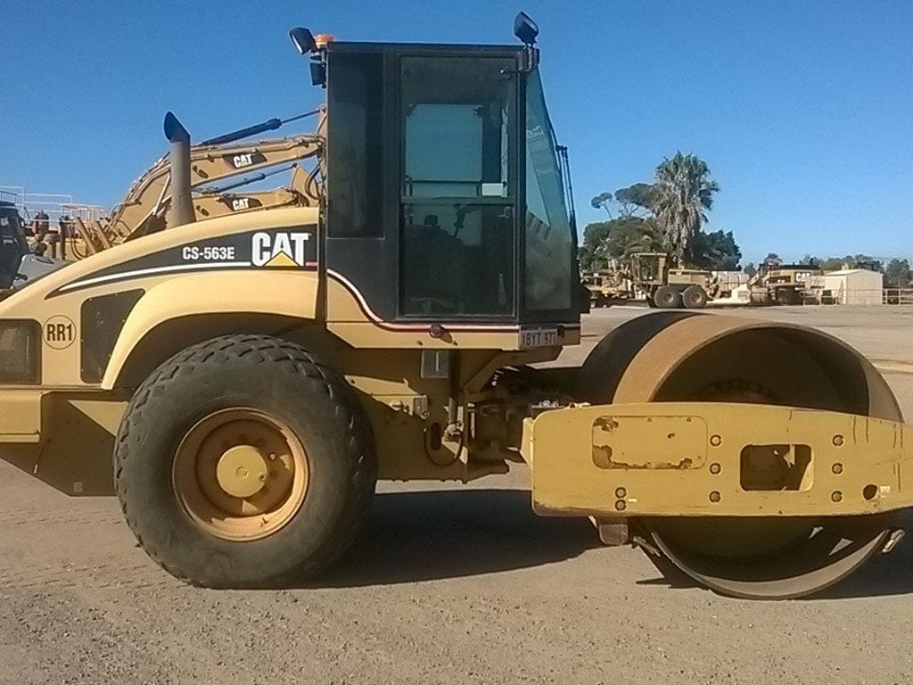 Cat CS-563E smooth drum vibratory roller parked in the yard with trucks behind