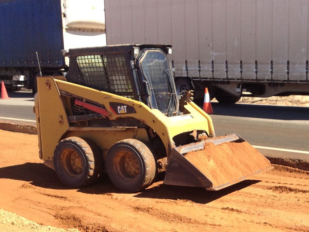 Cat skid steer loader on a red dirt road verge with a road train trailer behind