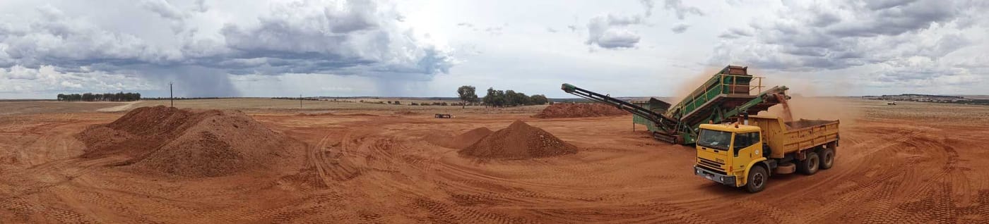 Crushing and screening plant loading a yellow truck beside sand stockpiles