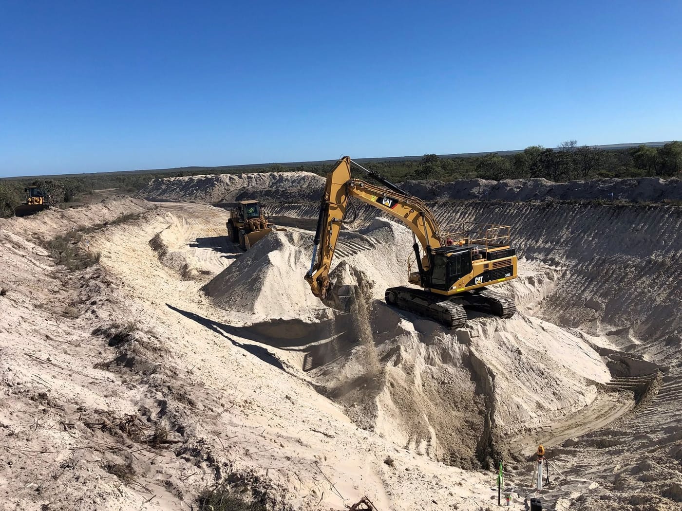 Drone view of a Lenane Holdings Cat excavator loading in a white limestone pit, with a wheel loader on the haul road behind
