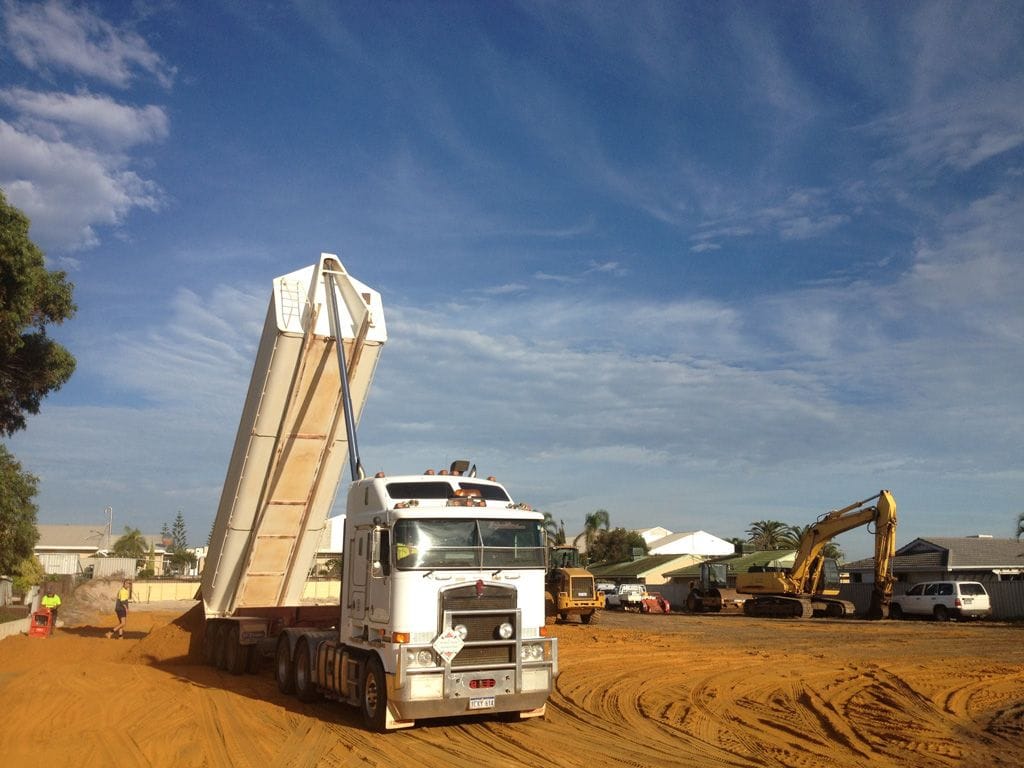 White Kenworth end tipper with its tray raised on site, excavator behind
