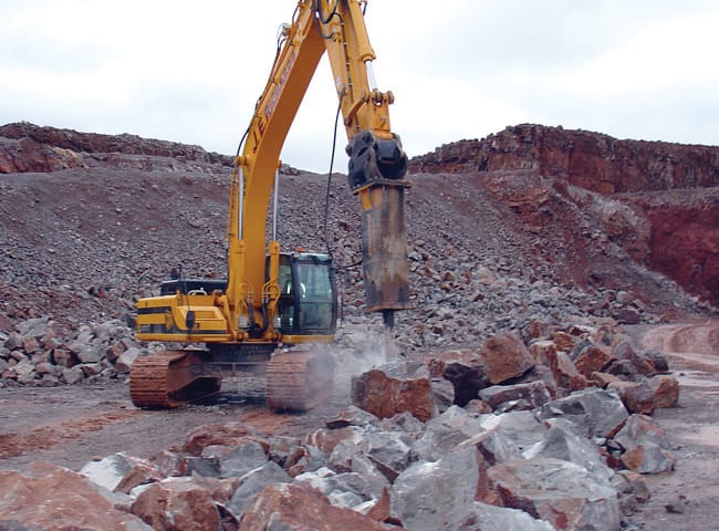 Excavator with a hydraulic rock breaker breaking rock at a quarry face
