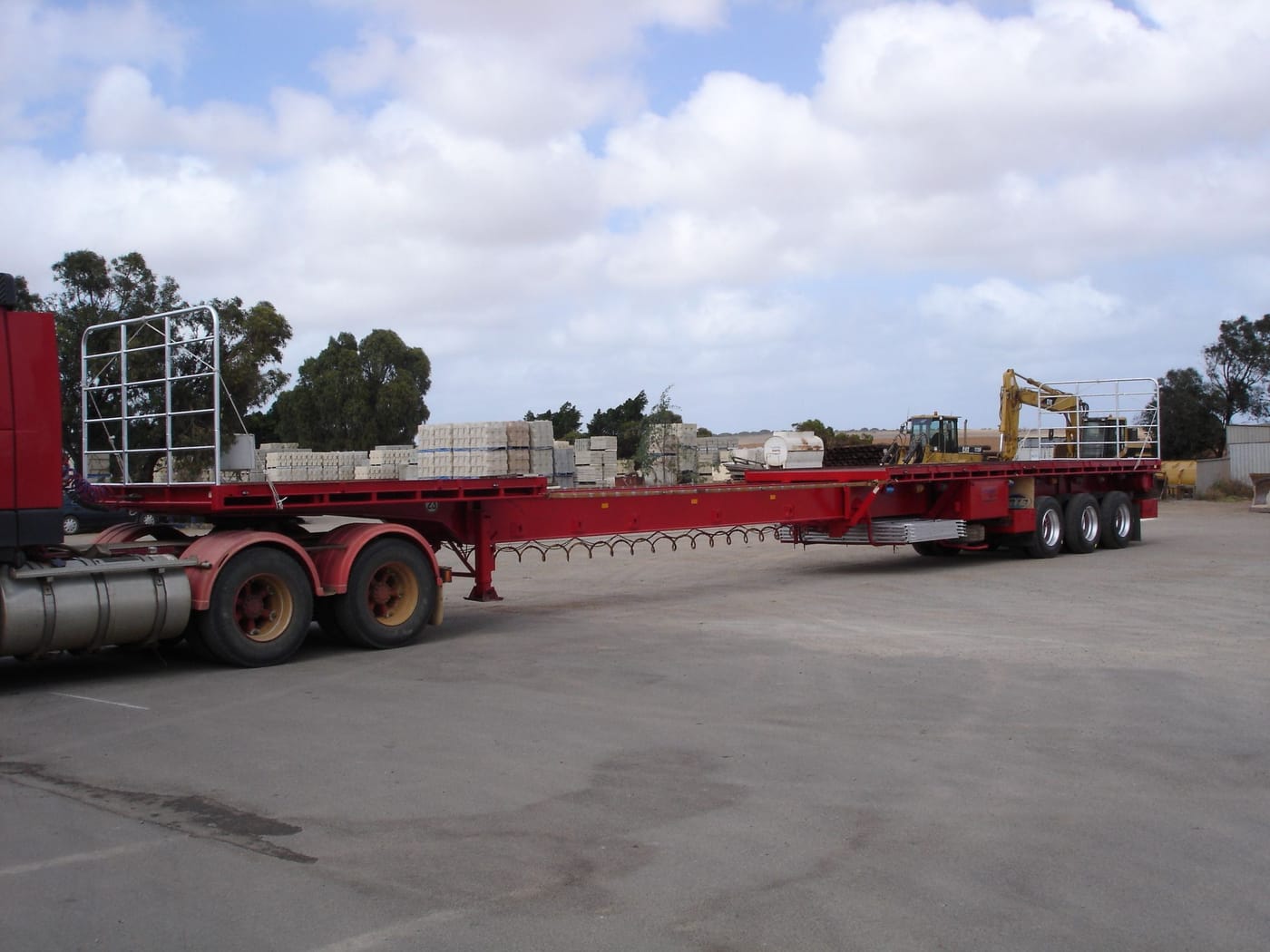 Red extendible flat top trailer in the Lenane yard with pallets and trees behind