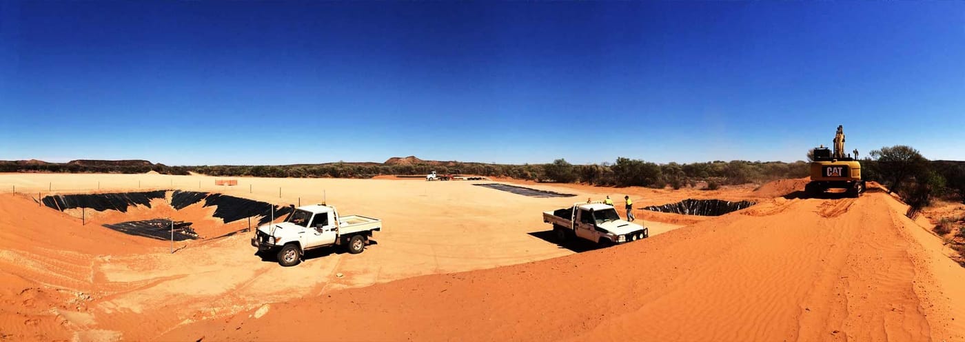Bright panorama of a lease site with utes, a water tank and a dozer on red dirt