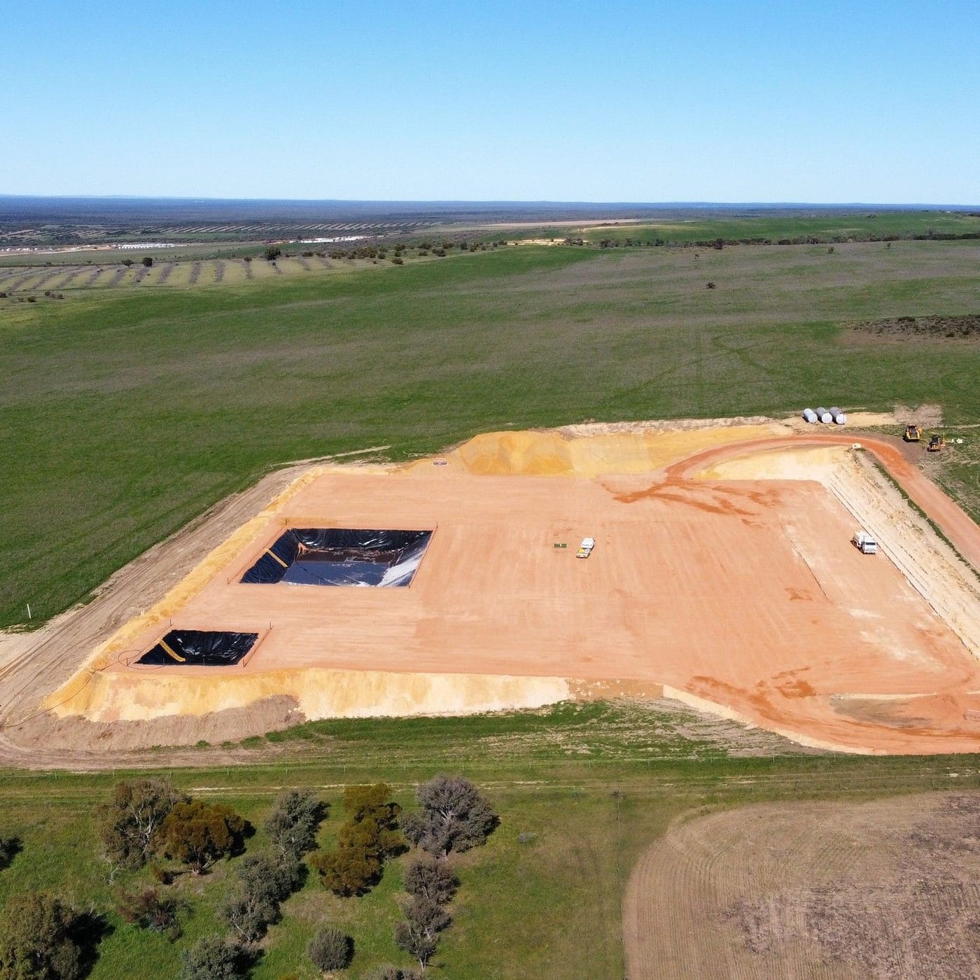 Drone view of a lined pad with sumps under construction, green paddocks either side