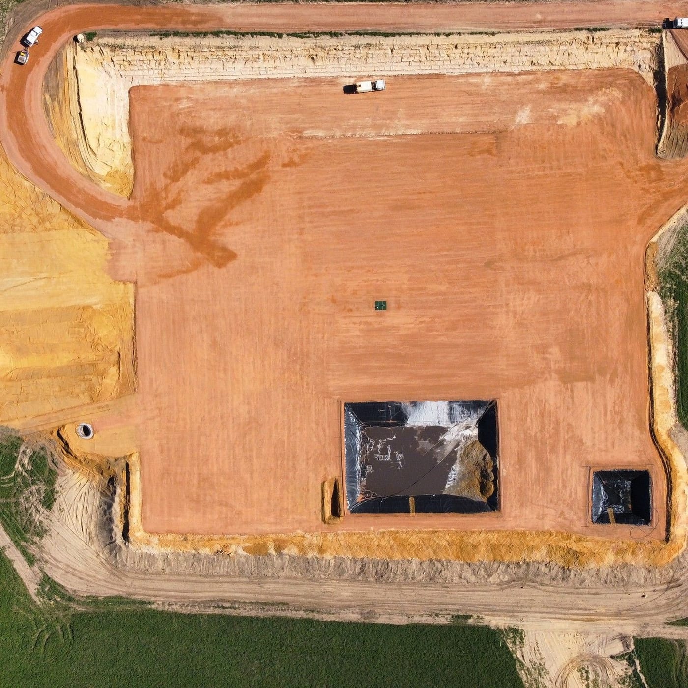 Drone view straight down onto a rectangular pad with lined sumps and a loader at work