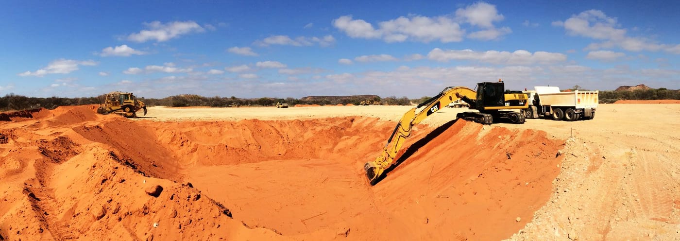 Cat excavator digging a large red dirt pit with a dozer, a loader and tipper trucks on the rim