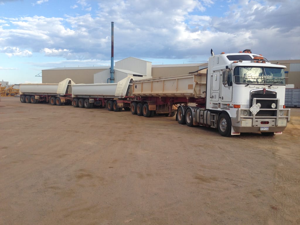 White Kenworth prime mover with a triple road train of side tippers in the yard