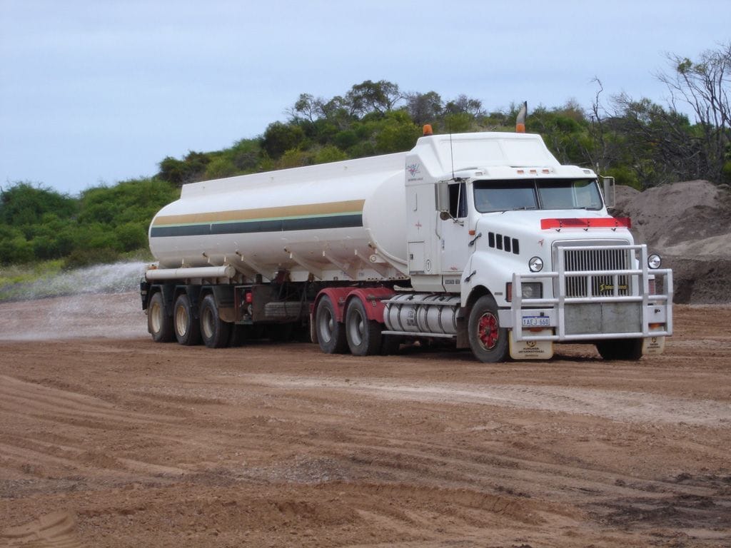 White Kenworth prime mover with a stainless water tanker semi on a dirt road